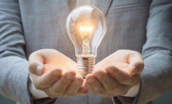 Person's hands gently holding a lit incandescent light bulb