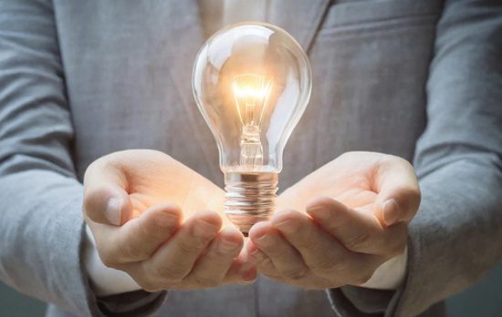 Person's hands gently holding a lit incandescent light bulb